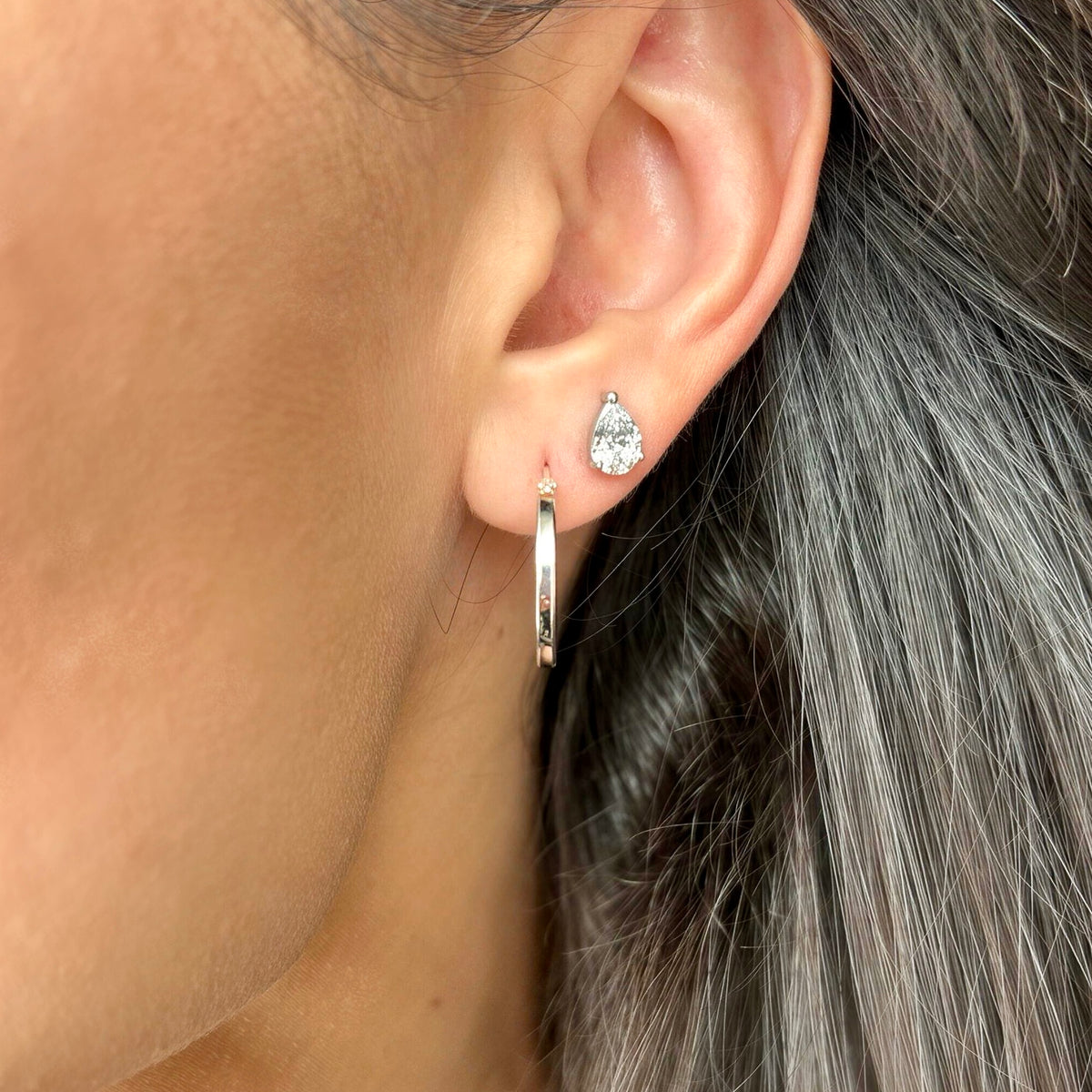 Silver hoop earring worn on ear, layered with stud earring