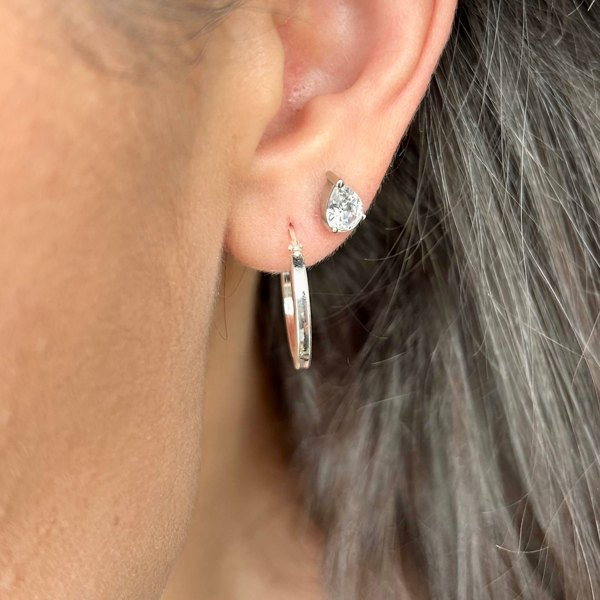 Close-up of silver hoop earring worn with diamond-style stud