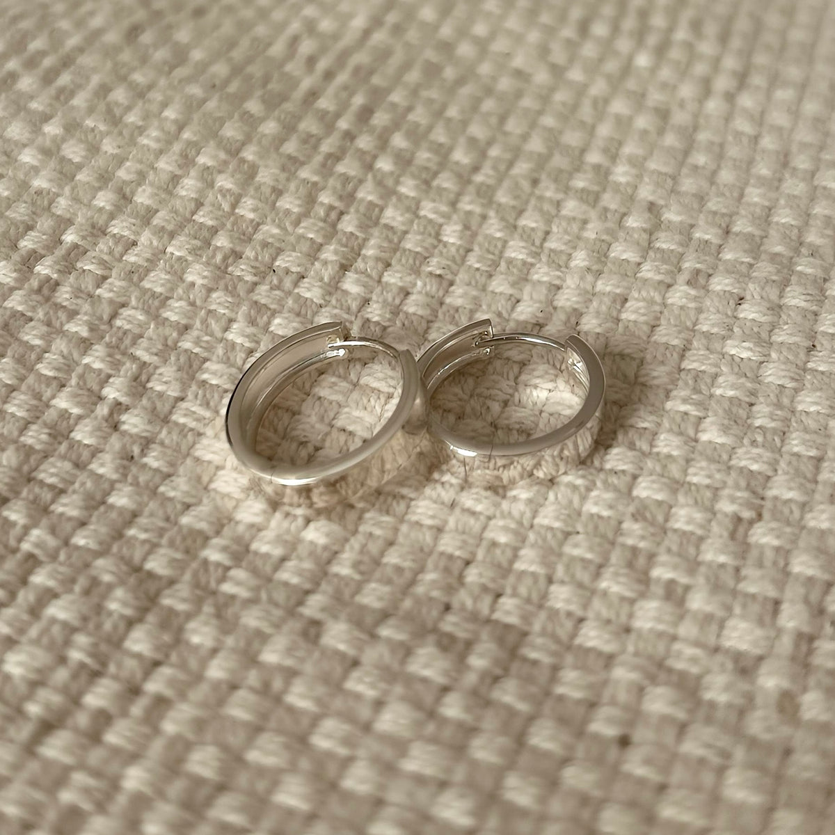Flat band silver hoop earrings on woven fabric, product photo