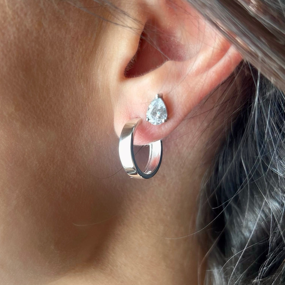 Close-up of silver hoop earring worn with diamond-style stud