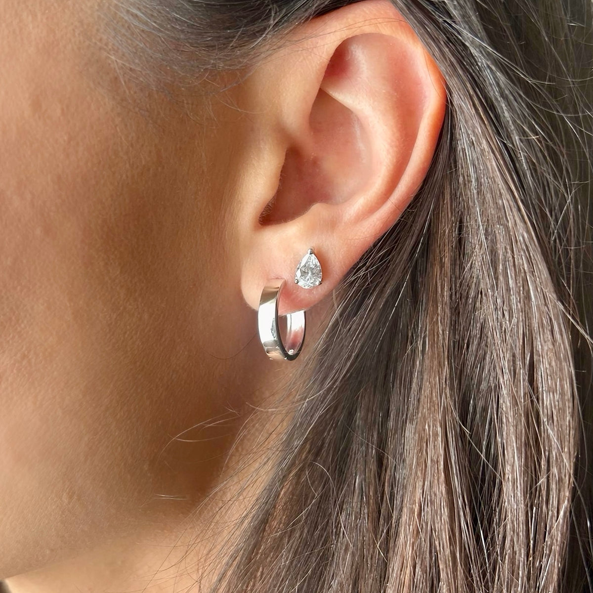 Silver hoop earring worn on ear, layered with stud earring